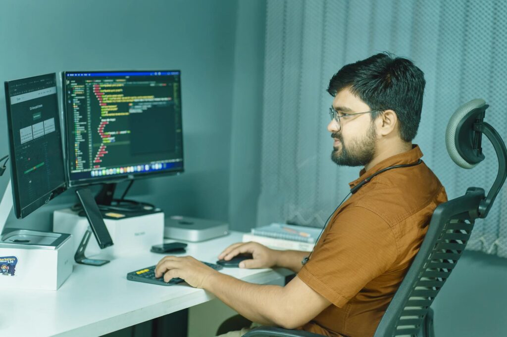 A Focused Developer Coding At A Modern Office With Dual Monitors, Showcasing A Tech-Driven Workspace.