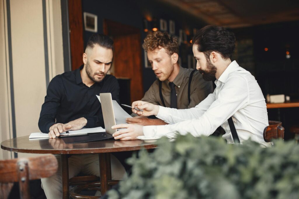 Three Young Men Collaborating In A Cozy Cafe Setting, Focused On A Laptop.