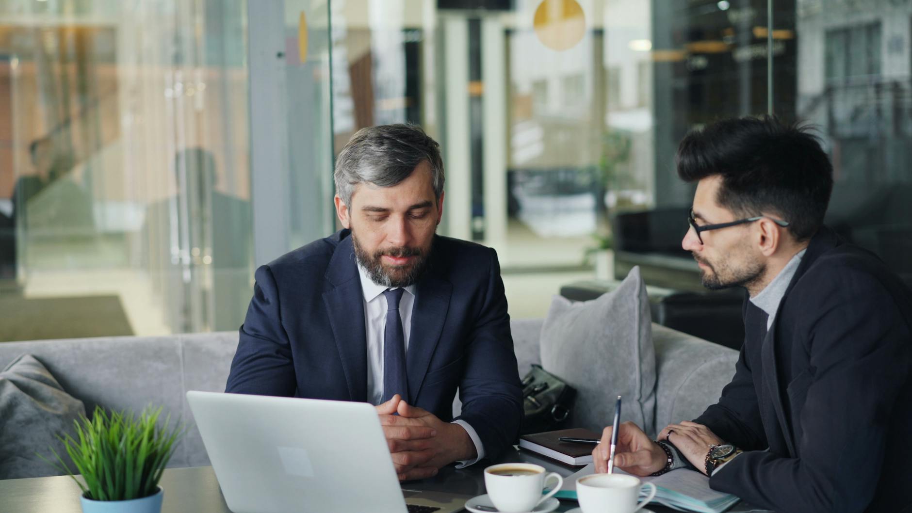 Two Businessmen In Suits Discussing Work At A Cafe 1