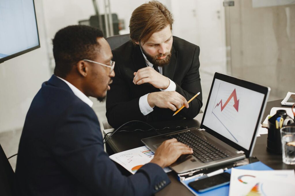 Two Business Professionals Discuss Marketing Data On A Laptop In A Modern Office.