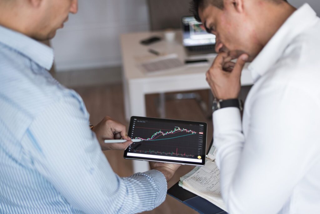 Two Businessmen Using A Tablet For Online Trading Analysis In An Office Setting.