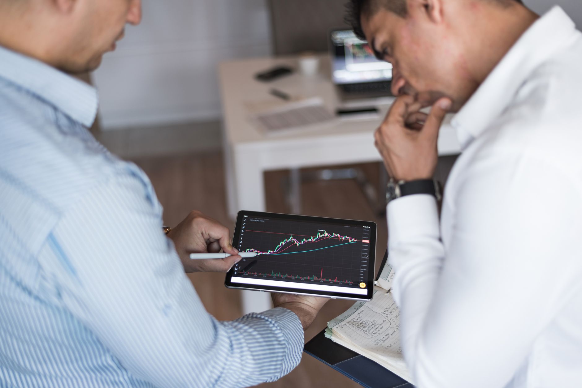 Two Businessmen Using A Tablet For Online Trading Analysis In An Office Setting.