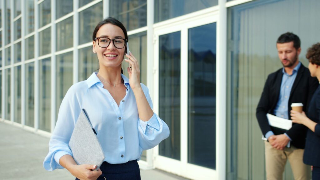 Confident Businesswoman Talking On Phone With Colleagues Outside Office Building.