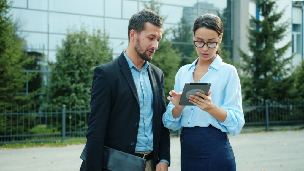 Professional Colleagues Discussing Work On A Tablet Outdoors In An Urban Setting.