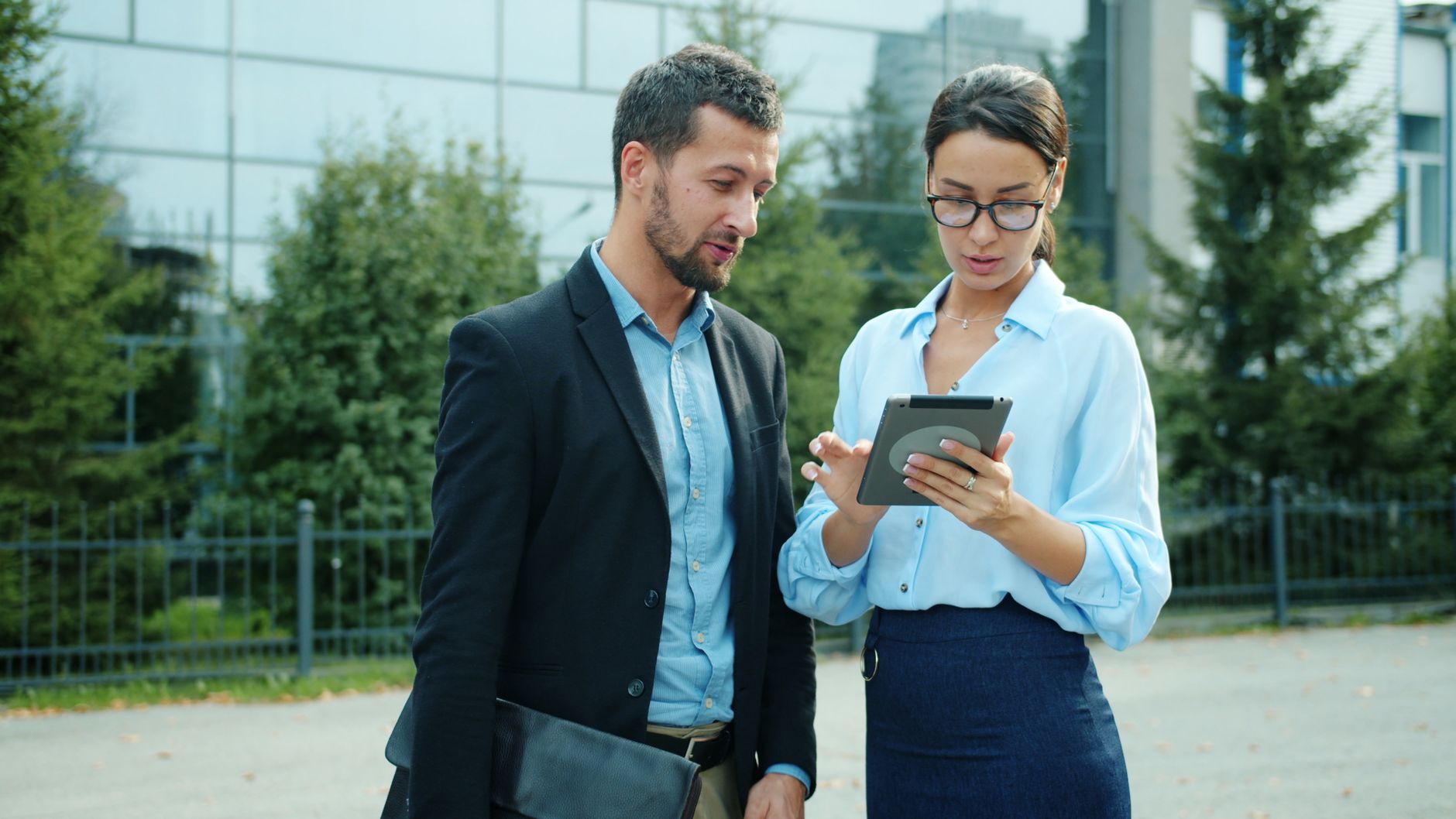 Professional Colleagues Discussing Work On A Tablet Outdoors In An Urban Setting.