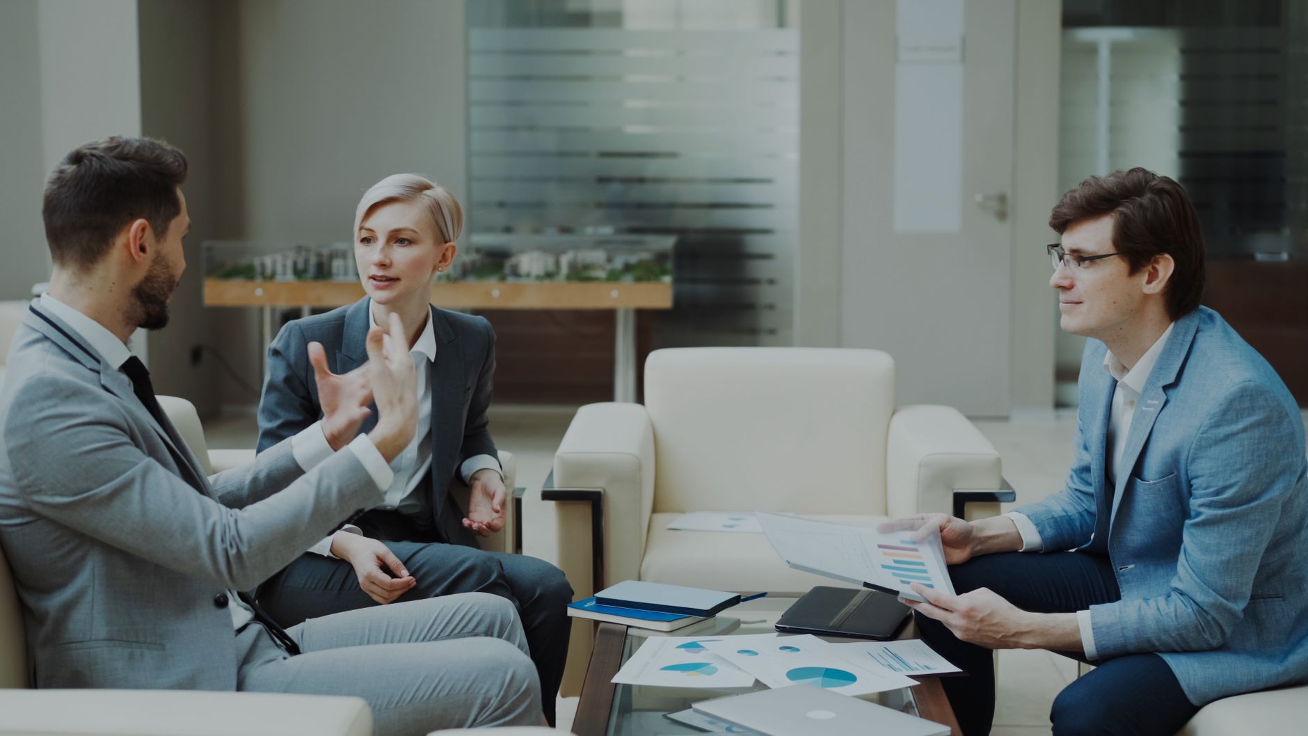 Three Professionals Engaged In A Meeting With Documents And Charts In A Modern Office.